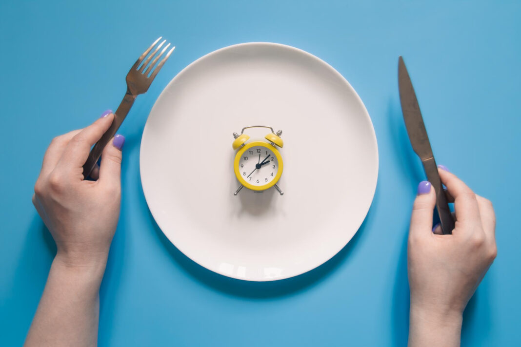 hands holding knife fork alarm clock plate blue background